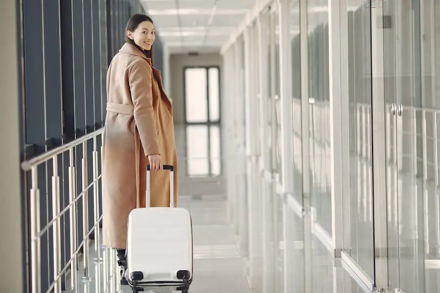 A cheerful woman in a stylish coat walks through an airport terminal with her suitcase.